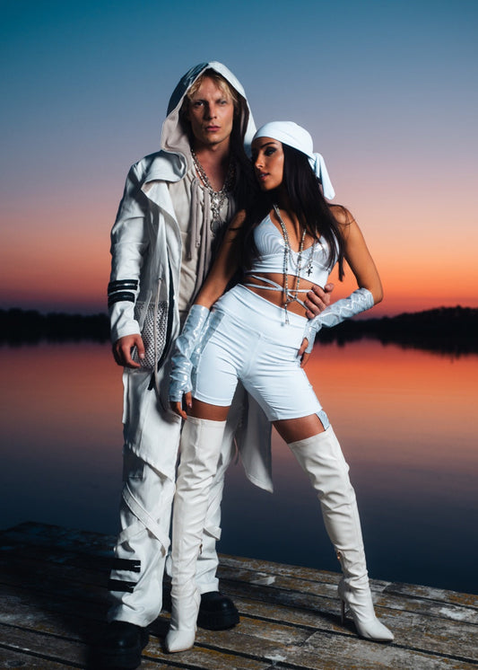 Two people in futuristic outfits standing on a dock at sunset.
