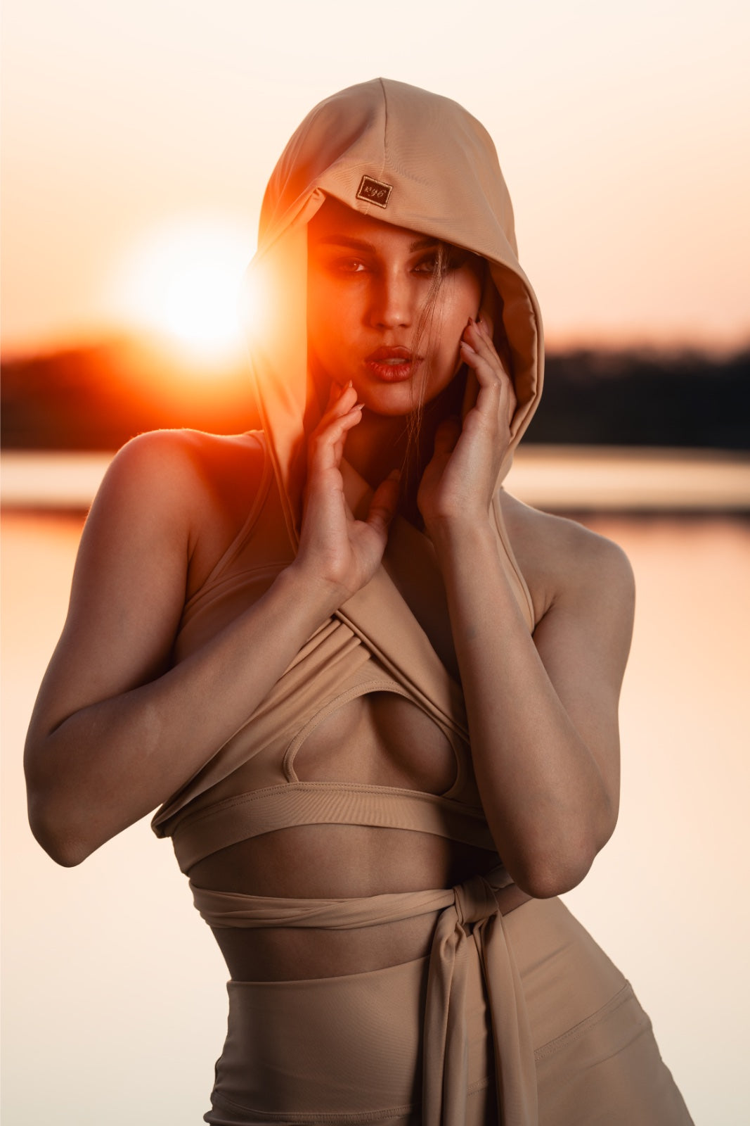 Woman in a beige outfit with a hood against a sunset background