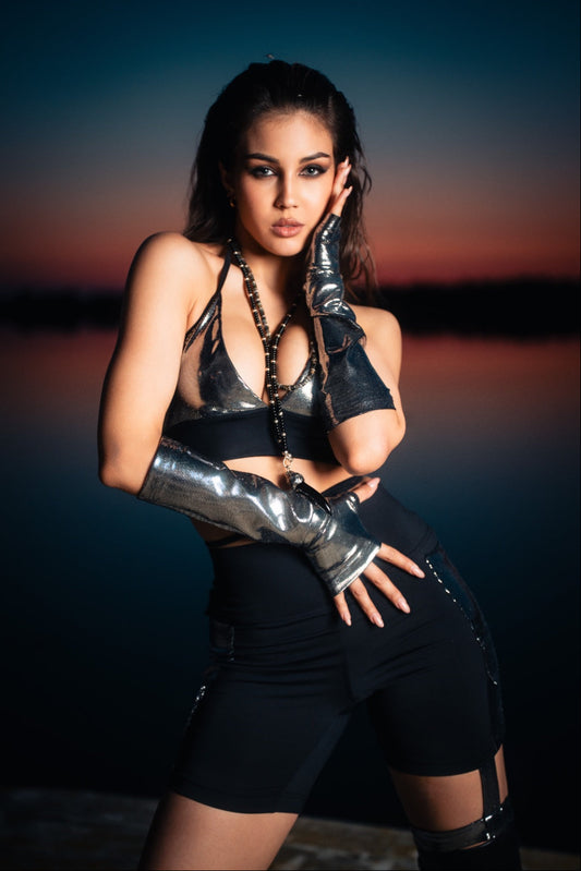 Woman in black outfit with metallic gloves against a sunset background