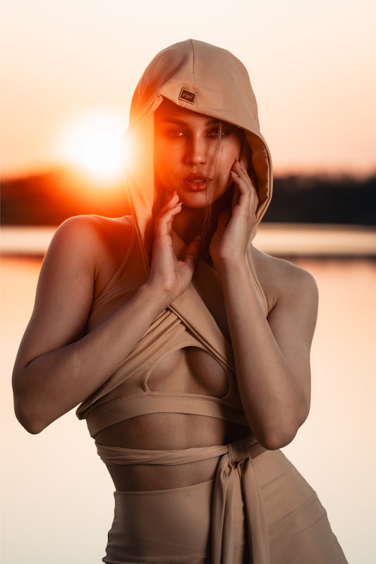Woman in a beige outfit with a hood against a sunset background