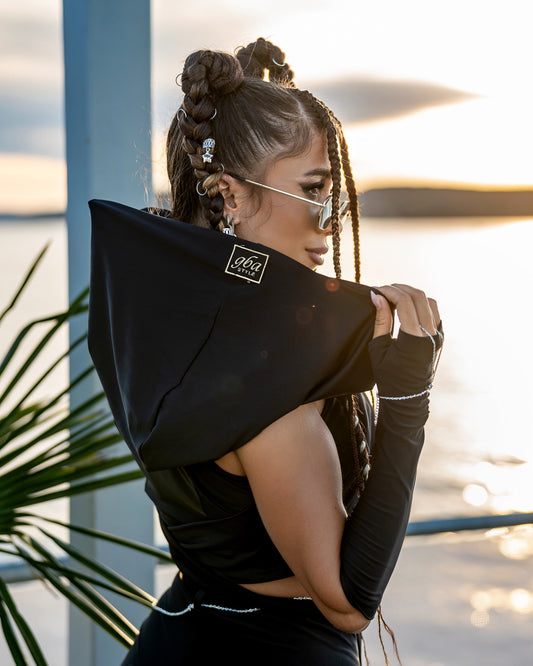 Woman wearing a black outfit with a brand logo, standing outdoors with a blurred background
