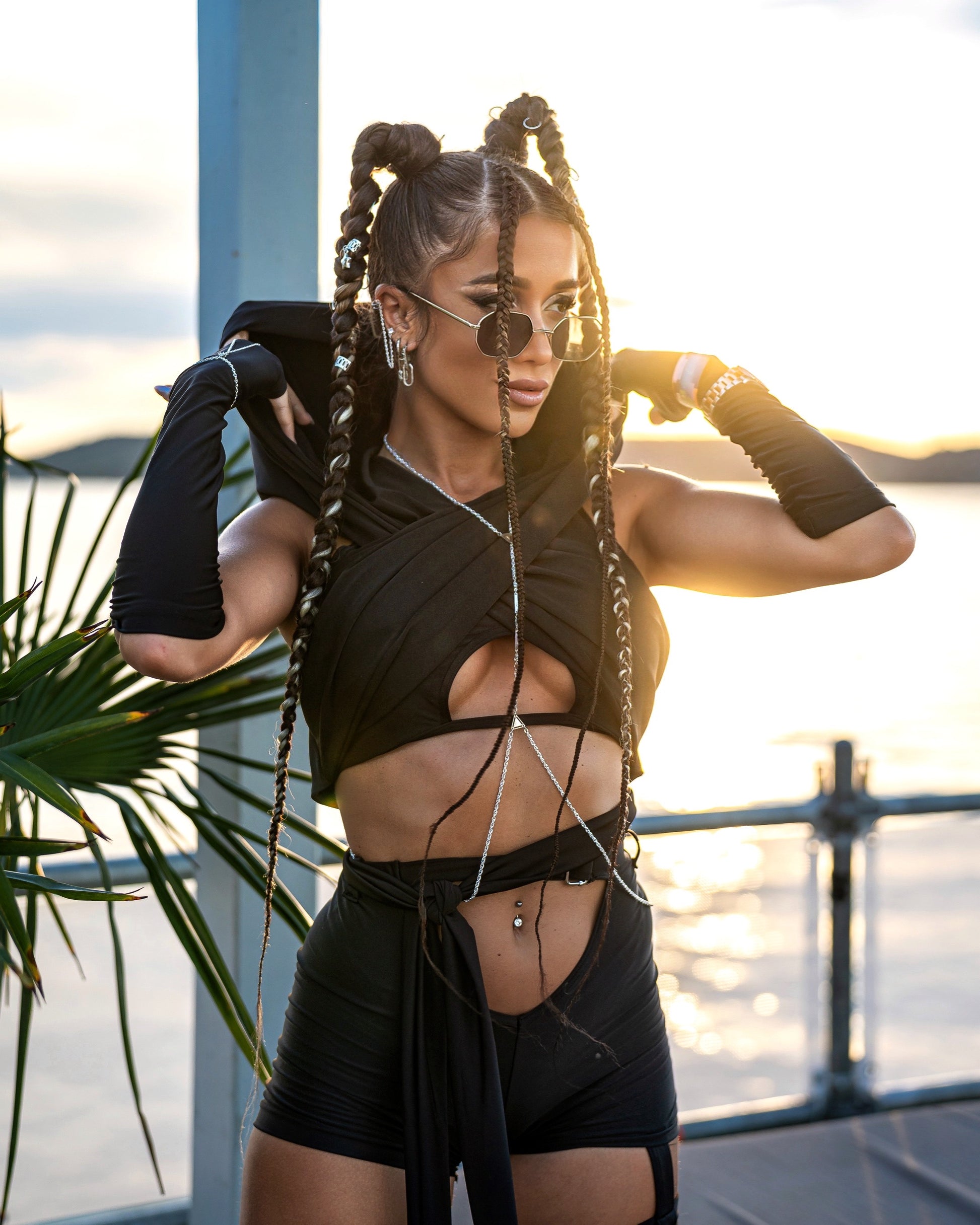 Woman in black outfit with braided hair by water at sunset